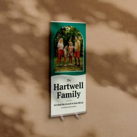 A retractable banner stand, 33 by 80 inches, against a warm plaster wall, printed with a family photograph and the words The Hartwell Family