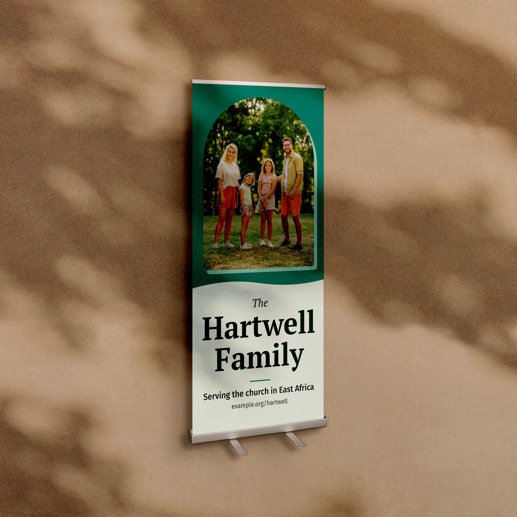 A retractable banner stand, 33 by 80 inches, against a warm plaster wall, printed with a family photograph and the words The Hartwell Family