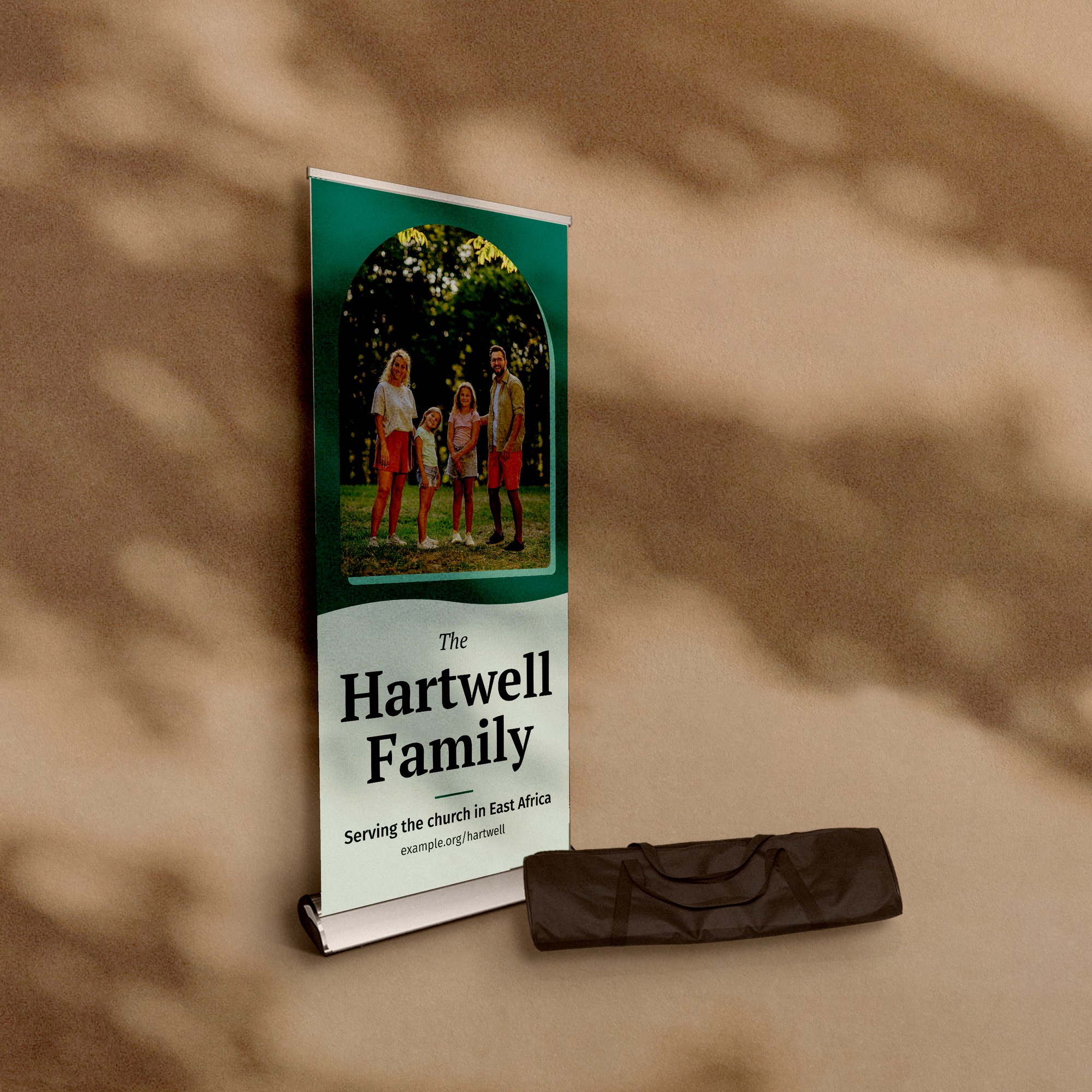 A Deluxe retractable banner stand, 33 by 80 inches, with its carrying bag beside it, against a warm plaster wall, printed with a family photograph and the words The Hartwell Family