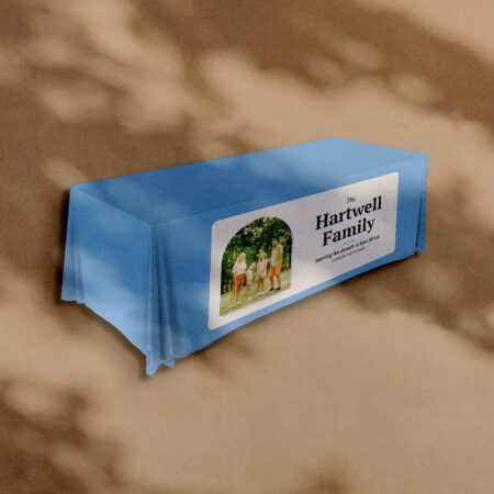 A printed tablecloth in light blue with a family photograph and the words The Hartwell Family on the front of the table, against a warm plaster wall