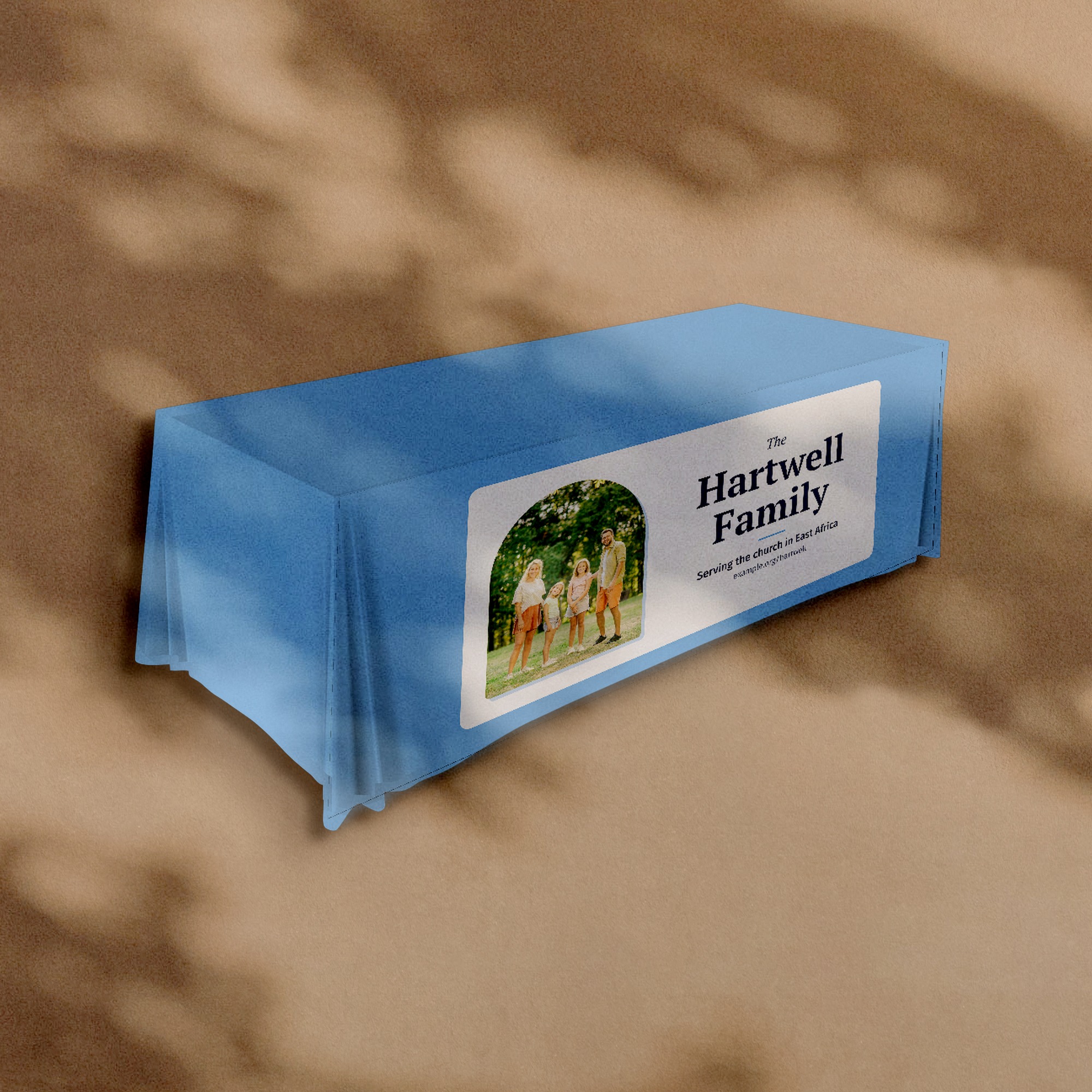 A printed tablecloth in light blue with a family photograph and the words The Hartwell Family on the front of the table, against a warm plaster wall