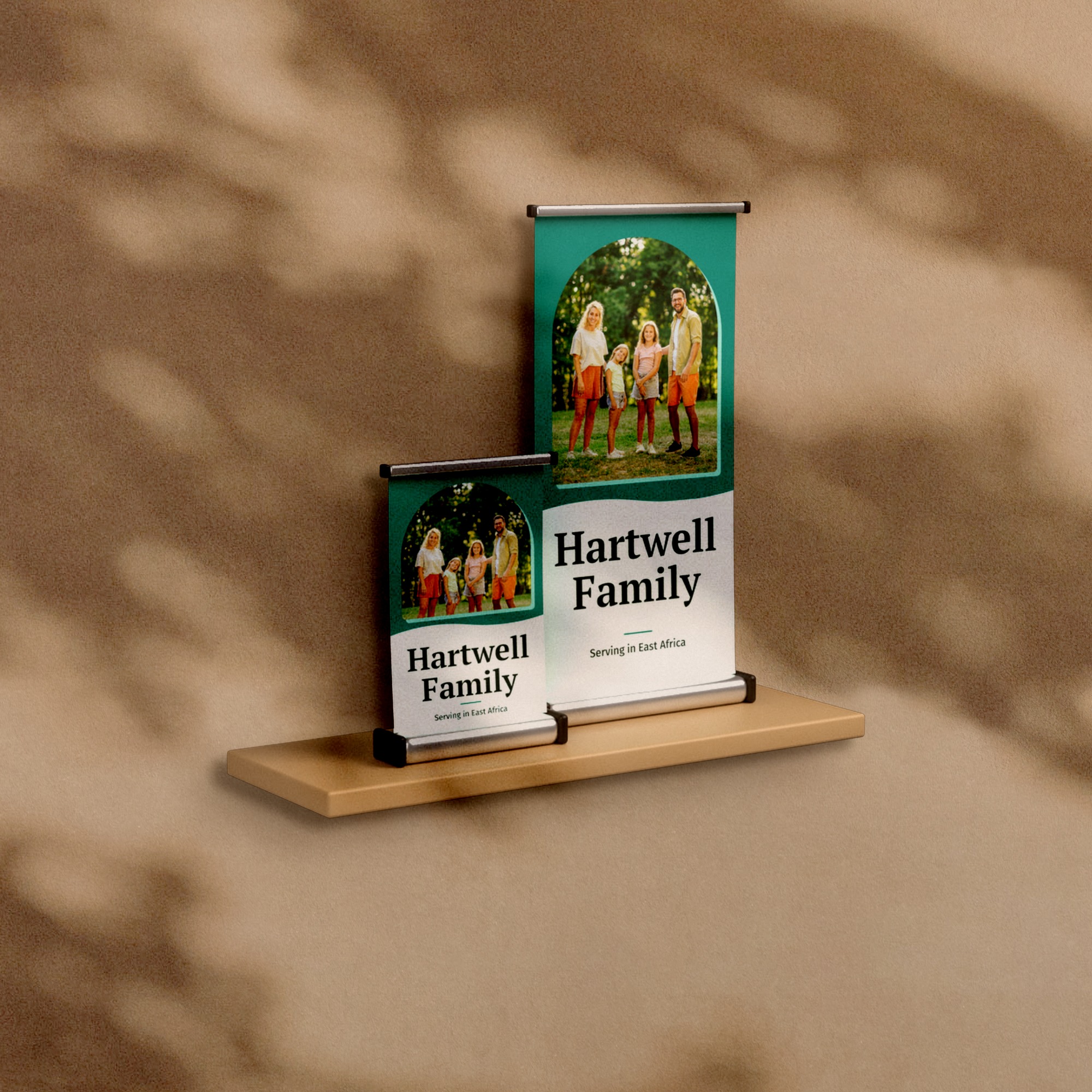 Two tabletop retractable banners, 15.75 by 32 inches and 11 by 17 inches, on a shelf against a warm plaster wall, printed with a family photograph and the words Hartwell Family